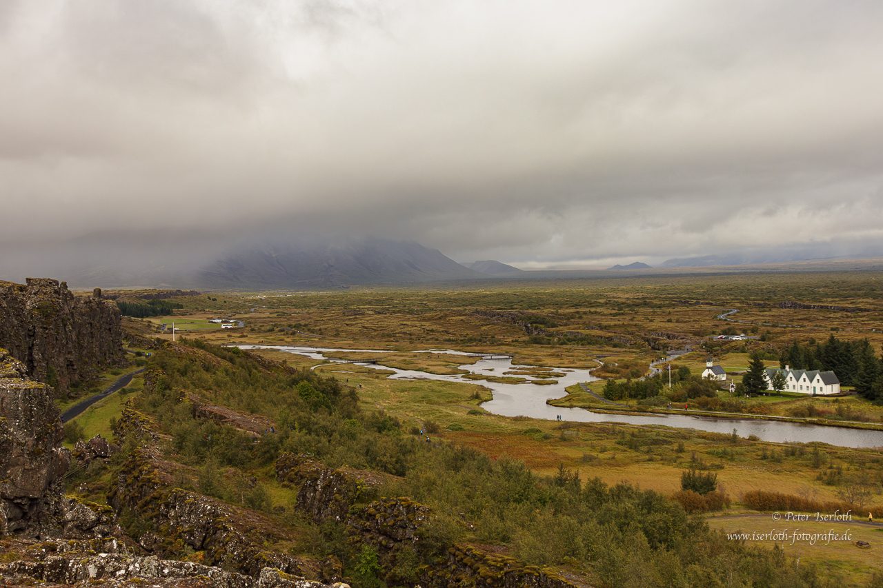 Landschaft auf Island. Landschaft mit Fluss, Wiesen und bewölktem Himmel, im Hintergrund Berge.